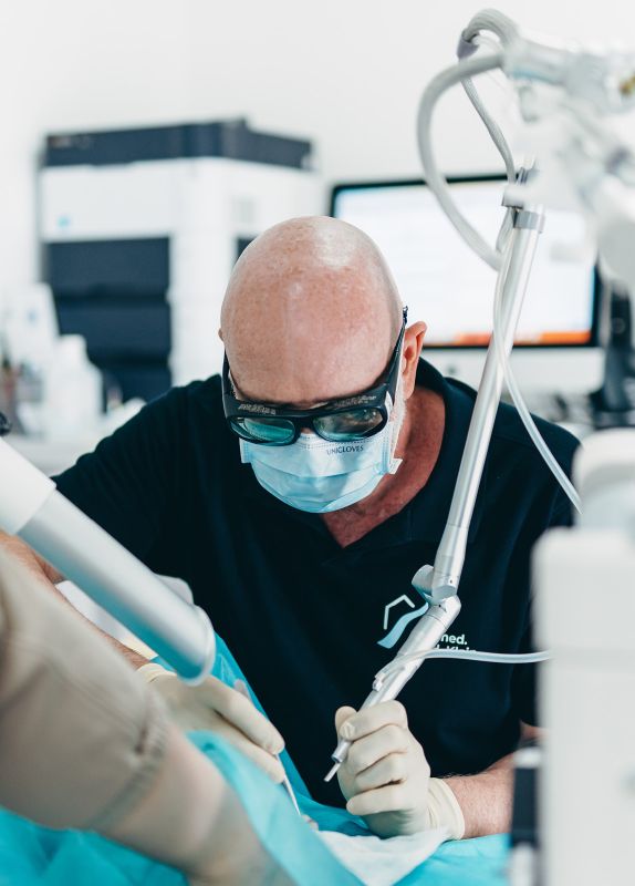 Herr Dr. Klein ist in einer OP-Situation. Er trägt eine Schutzbrille, eine Maske und Handschuhe behandelt eine nicht sichtbare Person mit einem Laser.